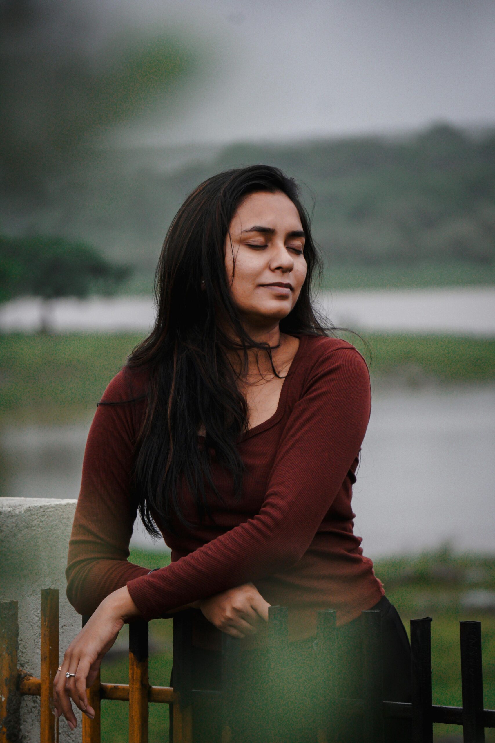Home A serene portrait of a woman posing by a scenic lake, exuding elegance and calmness.